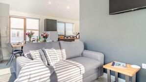 Ett modernt vardagsrum med en grå soffa, ett litet träbord och en tv som är monterad på väggen.