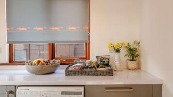Une cuisine équipée d’un lave-linge, avec un saladier rempli de fruits, un panier de collations et un vase de fleurs.