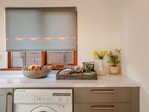A kitchen with a washing machine, a bowl of fruit, a basket of snacks, and a vase with flowers.