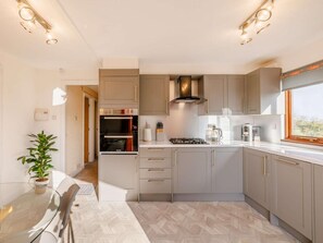 A modern kitchen with built-in appliances, a dining area with a glass table, and a view through a window.
