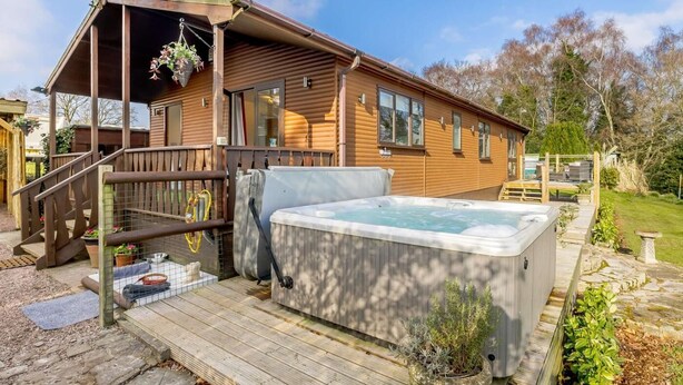 A wooden cabin with a hot tub, wooden deck, and a hanging plant. - 1 Bed in Northwich (oc-91266) (Foxwist Green)