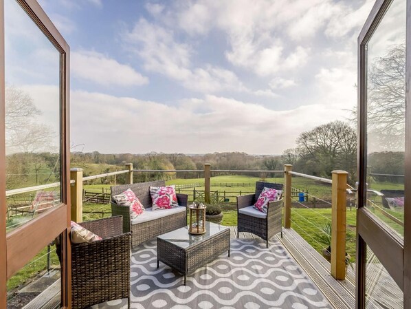 A balcony with wicker furniture, a glass table, and a view of the countryside.