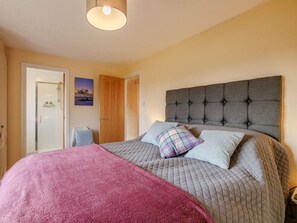 A bedroom with a large bed, a headboard, a door, and a wall-mounted picture.