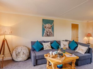 A living room with a grey sofa, teal cushions, a coffee table with a tray of cookies, a lamp, and a painting of a dog.