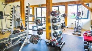 Ett gym med utrustning för styrketräning, konditionsmaskiner och stora fönster.