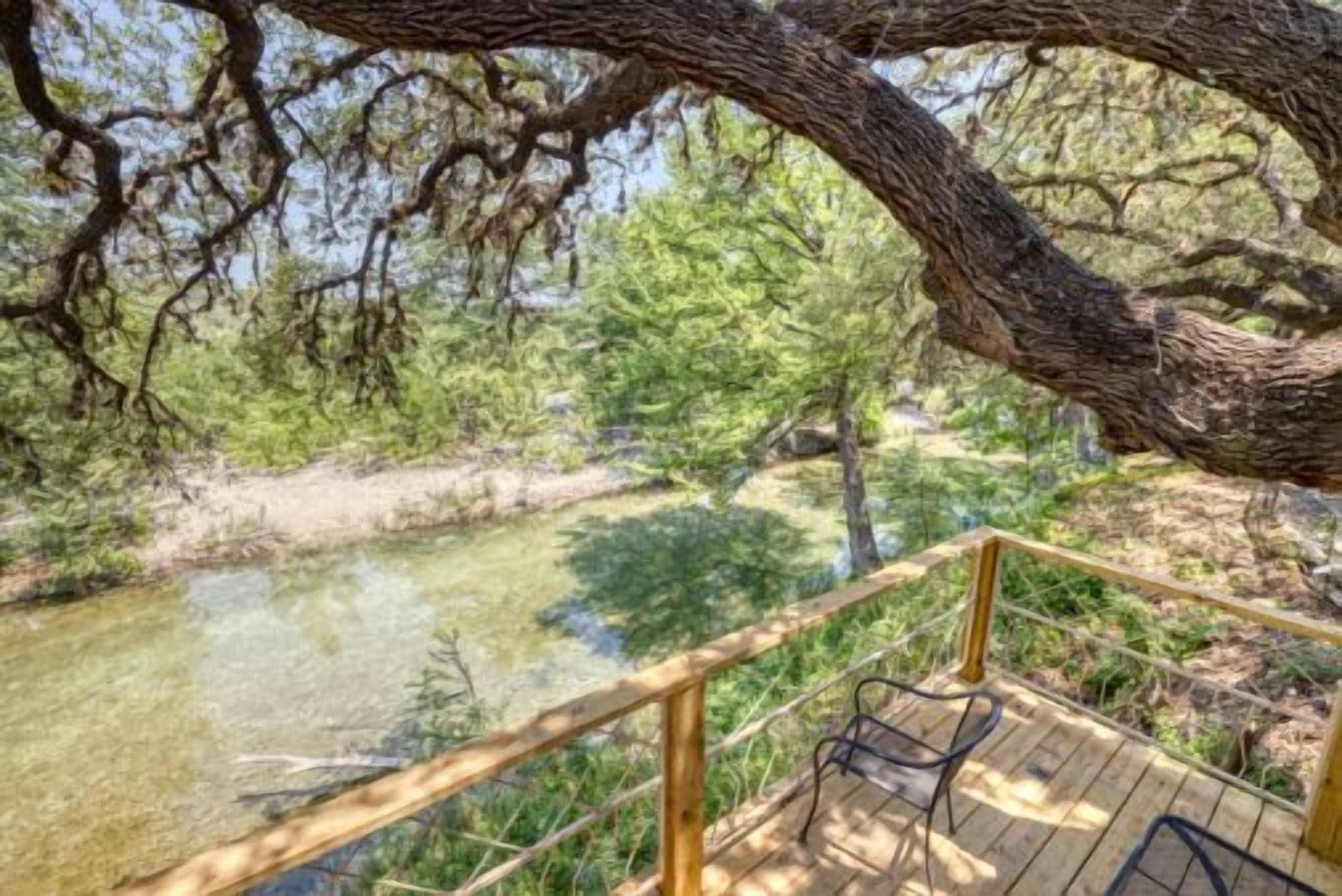Eine Holzterrasse mit Geländer, die auf einen Fluss mit umliegenden Bäumen blickt.