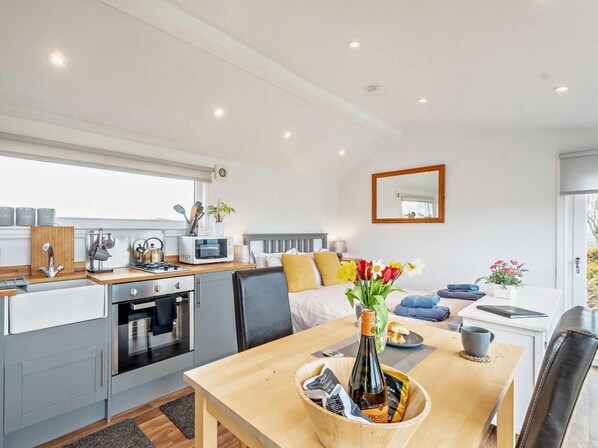 A modern kitchen with a microwave, stove, and sink. There's a dining table with a vase of flowers and a bottle of wine.