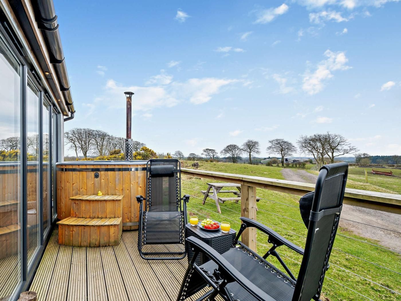 A deck with outdoor seating, a hot tub, and a view of the countryside.