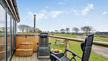 A deck with outdoor seating, a hot tub, and a view of the countryside.