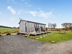 A rustic wooden cabin with a deck, a chimney, and a bench in a rural setting.