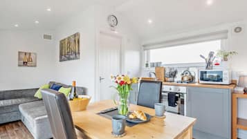 A modern kitchen with a microwave, stove, and sink. There is a dining table with a vase of flowers and a croissant. A gray sofa is in the living area.
