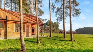 Punaisella katolla varustettu puinen mökki, jonka ympärillä on ruohokenttä ja korkeita puita.