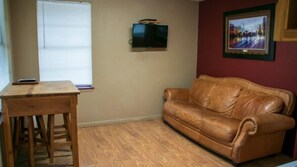 Una habitació amb taula de fusta, sofà de cuir, televisió penjada a la paret i un quadre amb marc.