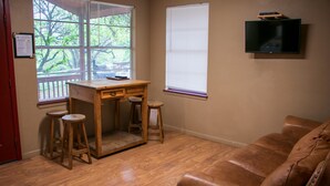 A small room with a wooden desk, two stools, a television, and a window with blinds. - Riverfront Cabins  and  Vacation Homes (Rio Frio)