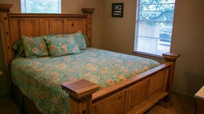 A wooden bed with a floral bedspread, a nightstand, and a window with blinds. - Riverfront Cabins  and  Vacation Homes (Rio Frio)
