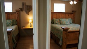 A bedroom with two wooden beds, a nightstand, a lamp, and a window. - Riverfront Cabins  and  Vacation Homes (Rio Frio)