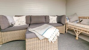 Ein Eckzimmer mit einem grauen Ecksofa, einem Korbstuhl und einem gewebten Hocker.