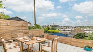Eine Terrasse mit Tisch und Stühlen, Blick auf eine Stadt und ein Holzzaun.