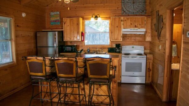 A wooden cabin kitchen with a refrigerator, stove, and bar stools. - Riverfront Cabins  and  Vacation Homes (Rio Frio)