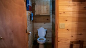A wooden cabin bathroom with a toilet, wooden walls, and a wooden cabinet. - Riverfront Cabins  and  Vacation Homes (Rio Frio)