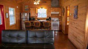 A wooden cabin interior with a dining area, kitchen, and a leather couch. - Riverfront Cabins  and  Vacation Homes (Rio Frio)