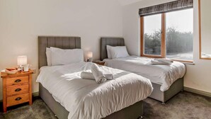A hotel room with two beds, a nightstand, a lamp, and a large window. - 3 Bed in King's Lynn (oc-91286) (North Runcton)