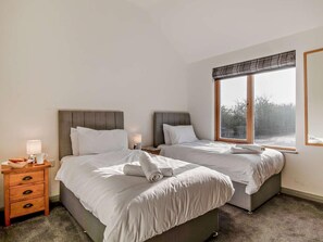 Ein Hotelzimmer mit zwei Betten, einem Nachttisch, einer Lampe und einem großen Fenster.