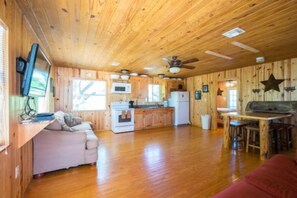 A cabin interior with a wooden ceiling, a kitchen area, a dining table, and a sofa. - Riverfront Cabins  and  Vacation Homes (Rio Frio)