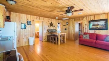 A wooden-paneled room with a ceiling fan, a red sofa, a dining table, and a kitchen area.