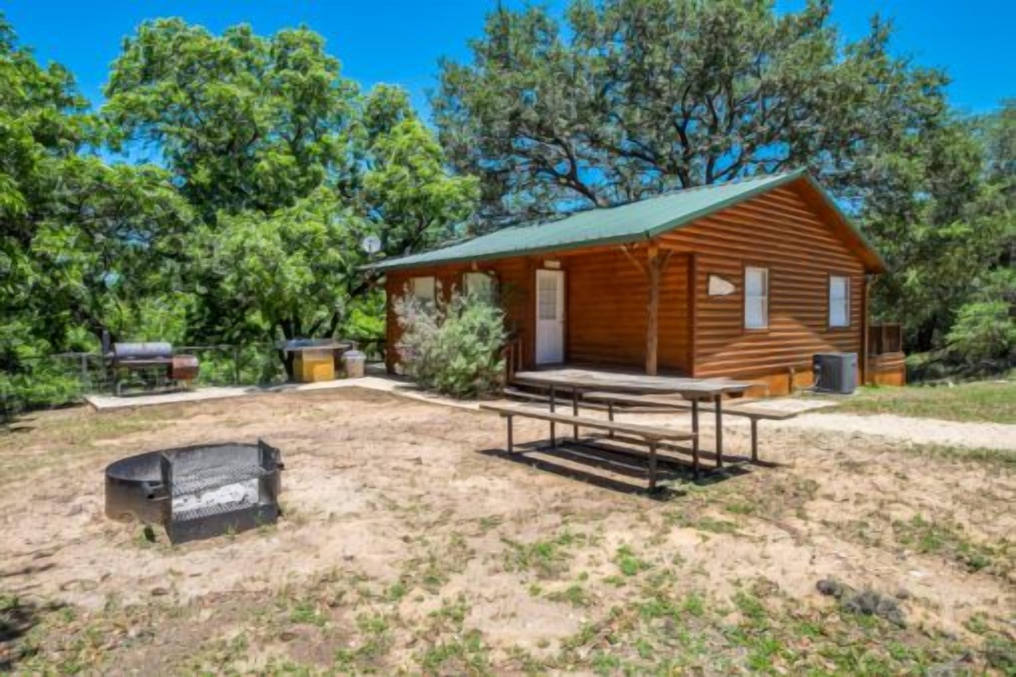 A rustic cabin with a porch, a picnic table, and a fire pit.