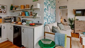 A modern kitchen with white cabinets, a built-in microwave, and a dishwasher. There is a dining area with a green chair and a white sofa.