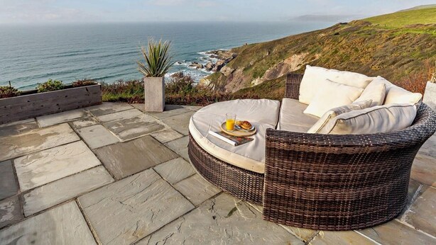 A wicker outdoor seating area with a cushion, a tray with a drink and a snack, and a potted plant.