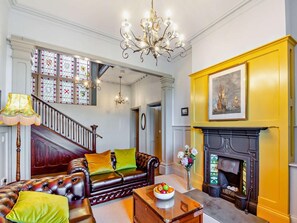 A traditional living room with a fireplace, a staircase, and a chandelier. - 9 Bed in Talsarnau (oc-90740) (Talsarnau)