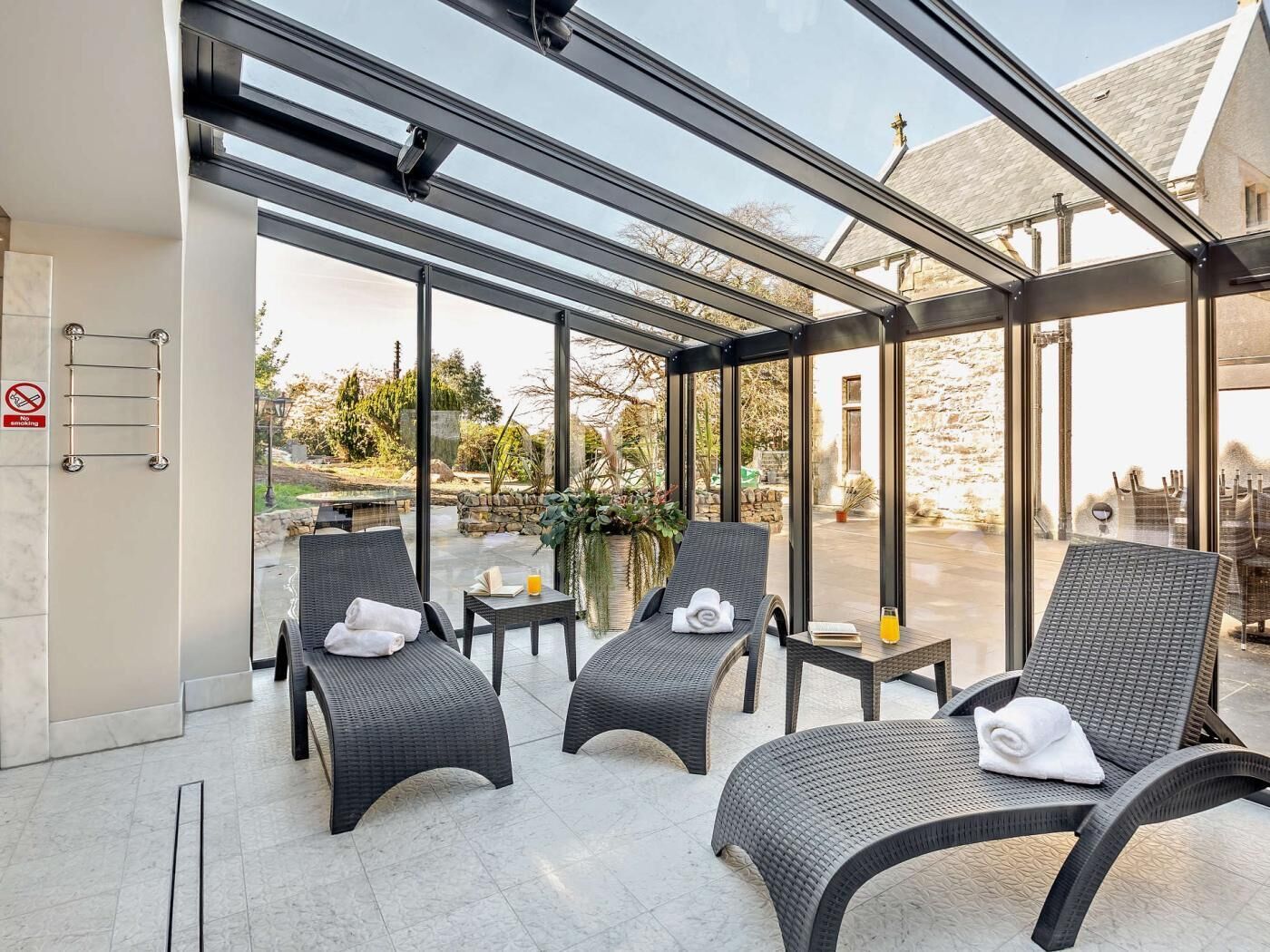 A glass-enclosed lounge area with wicker furniture and a view of the outdoor garden.