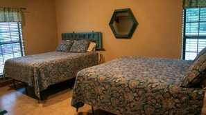 A bedroom with two beds, a hexagonal mirror, and a window with blinds.