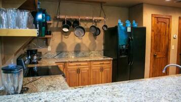 A kitchen with granite countertops, wooden cabinets, a black refrigerator, and hanging pots.