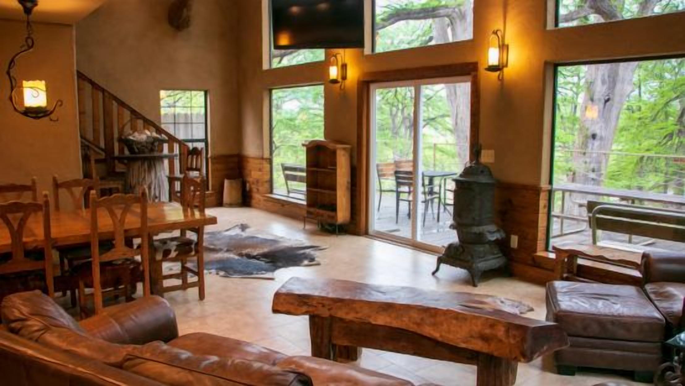 A spacious living area with a fireplace, wooden furniture, and large windows offering a view of the outdoors.