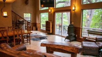 A spacious living area with a fireplace, wooden furniture, and large windows offering a view of the outdoors.