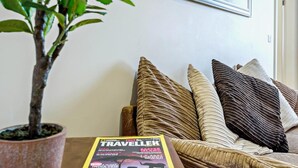 En stue med en sofa, puder, en potteplante, et indrammet billede og et magasin på bordet.