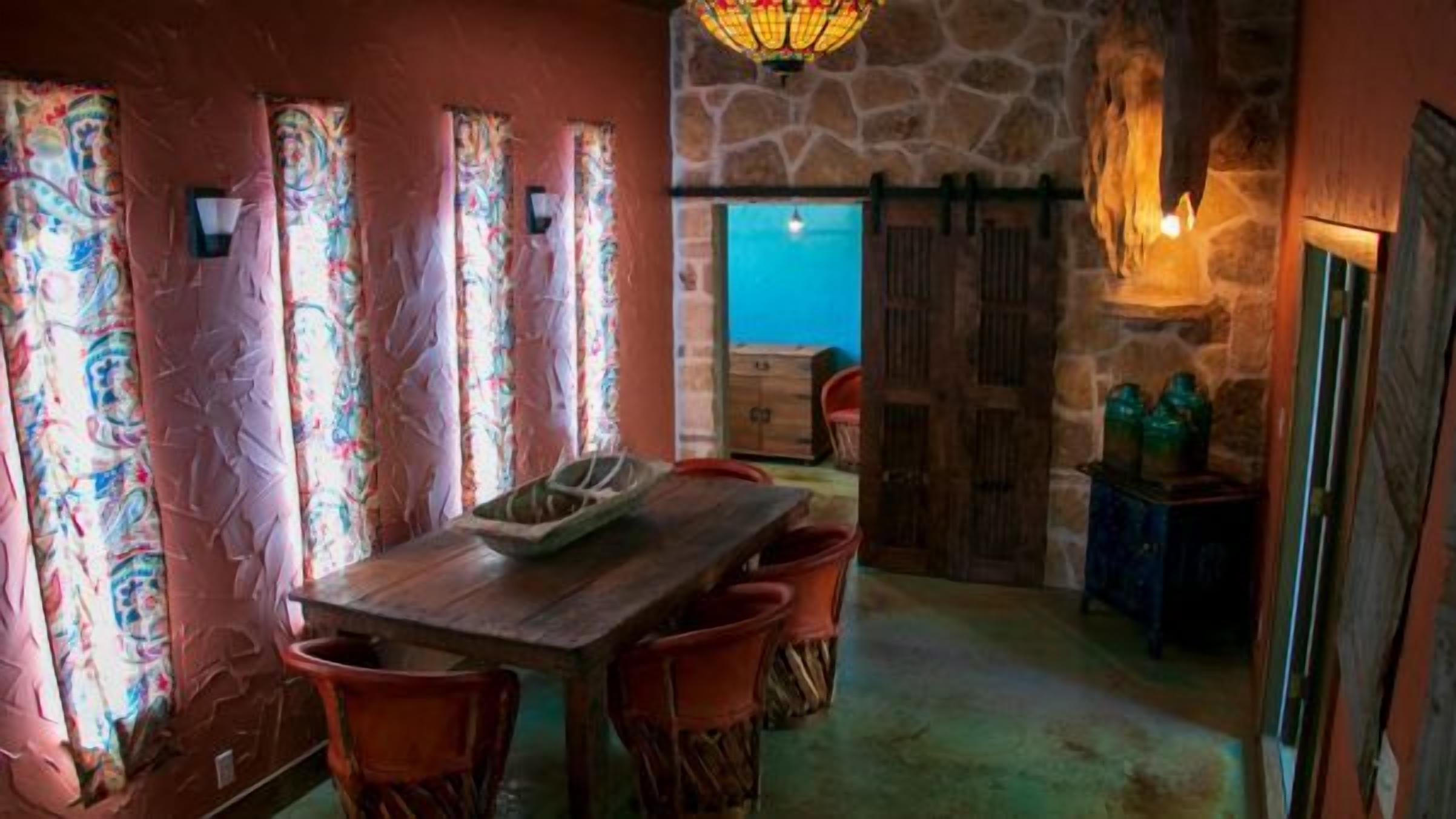 A dining area with a wooden table and chairs, a stone wall, and a view through a door.