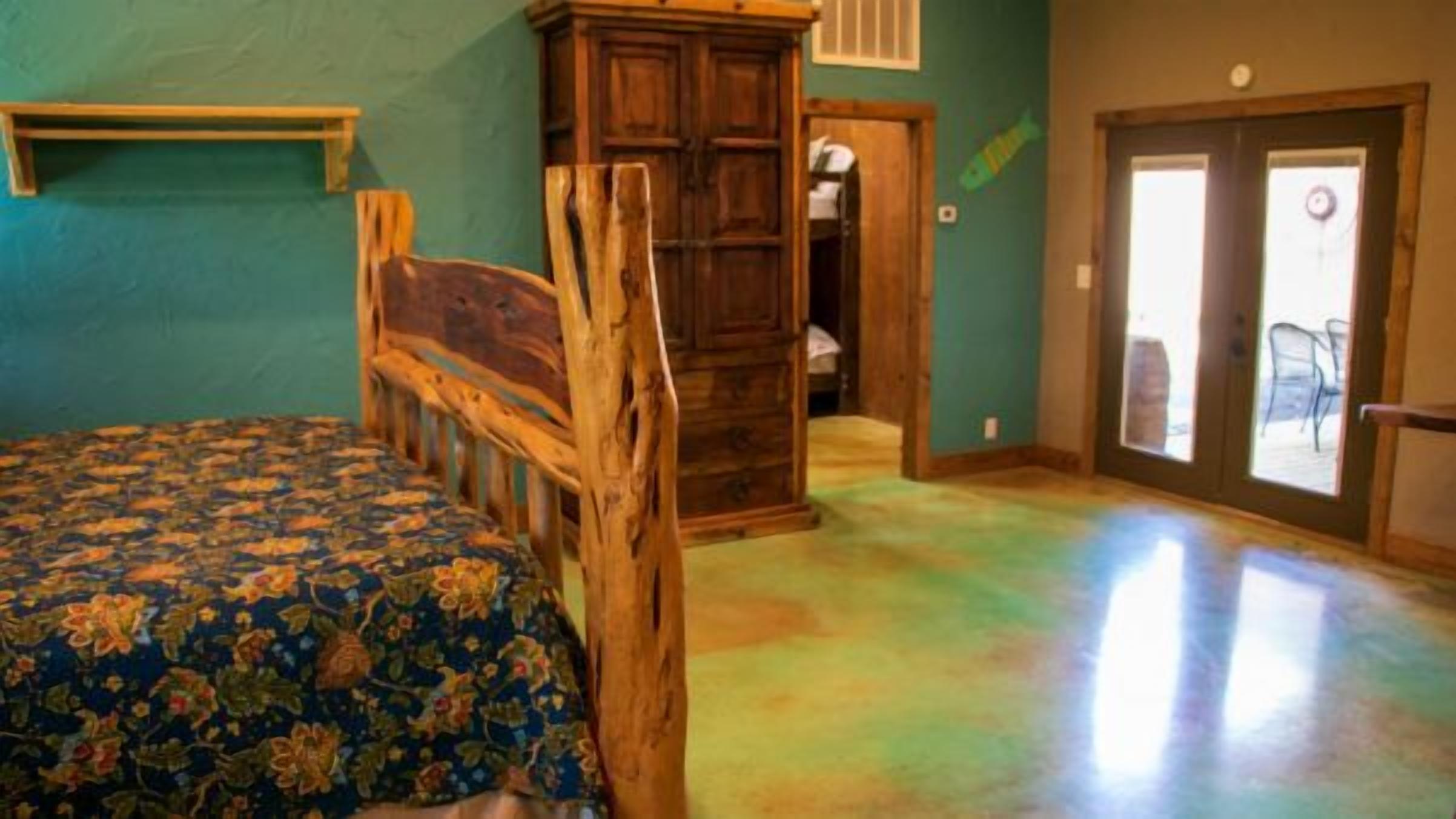 A bedroom with a wooden headboard, a bed with a floral bedspread, a wooden wardrobe, and a sliding glass door leading to an outdoor area.