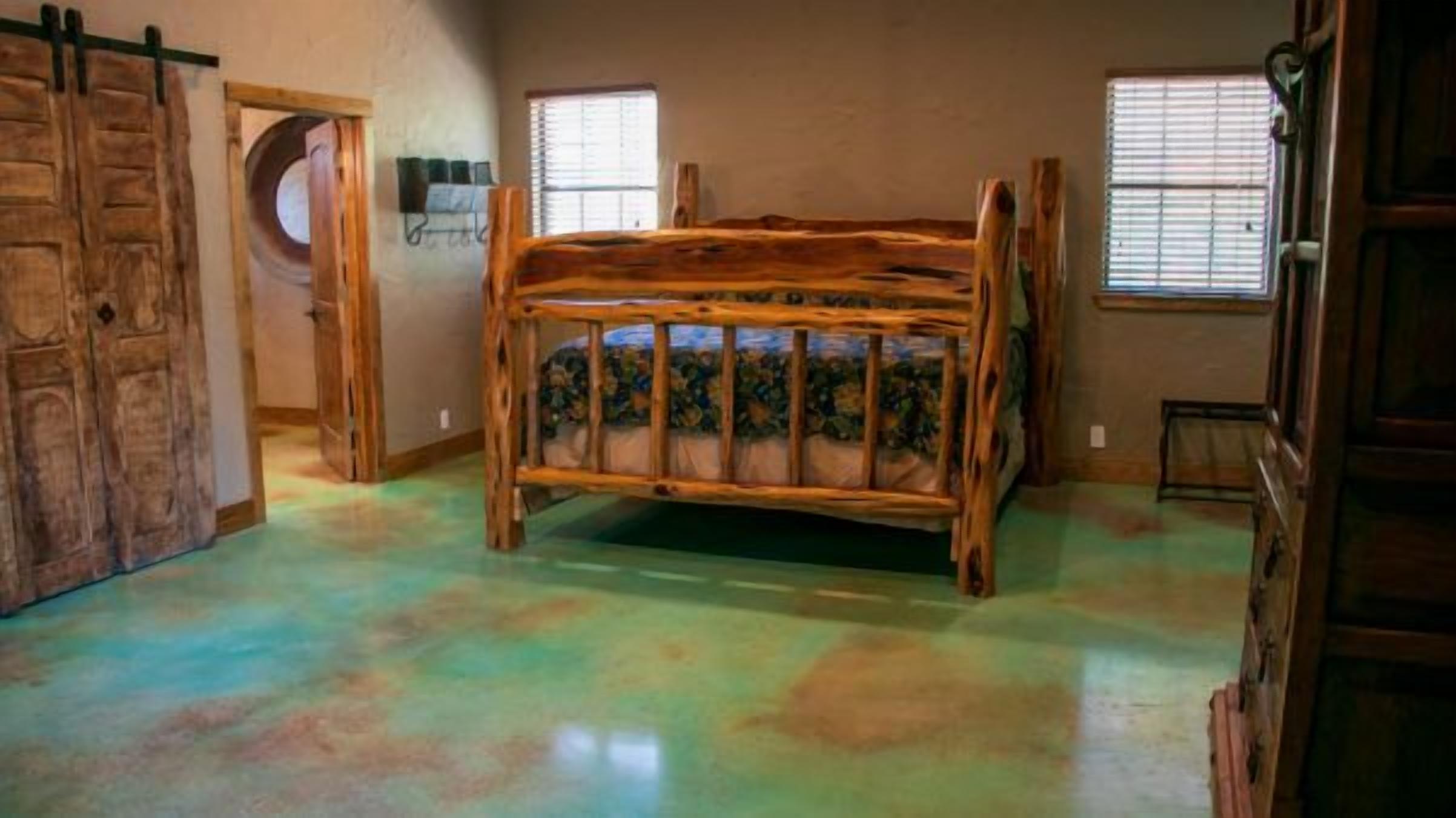 Una habitación con una cama de madera, un ventanal circular y una puerta.