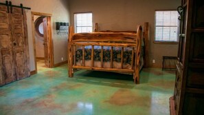 Una habitación con una cama de madera, un ventanal circular y una puerta.