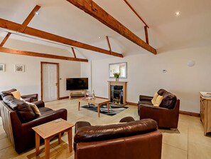 Ein großzügiges Wohnzimmer mit Kamin, Ledersofas, einem Fernseher und Holzbalken an der Decke.