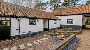 Een wit gebouw met twee verdiepingen, een dak van tegels, een grindpad en een kleine tuin met stenen en looppaden.