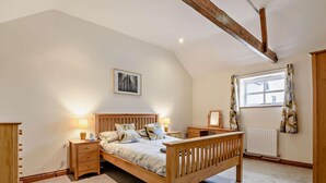 Een slaapkamer met een houten bed, nachtkastjes, een radiator, een raam met gordijnen, en een schilderij aan de muur.
