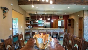 A dining area with a wooden table and chairs, a kitchen in the background, and a stone wall. - Riverfront Cabins  and  Vacation Homes (Rio Frio)