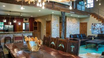 A spacious dining area with a long wooden table and chairs, a rustic stone wall, and a staircase leading to an upper level.
