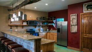 A kitchen with a bar area, wooden cabinets, a refrigerator, and a microwave. - Riverfront Cabins  and  Vacation Homes (Rio Frio)