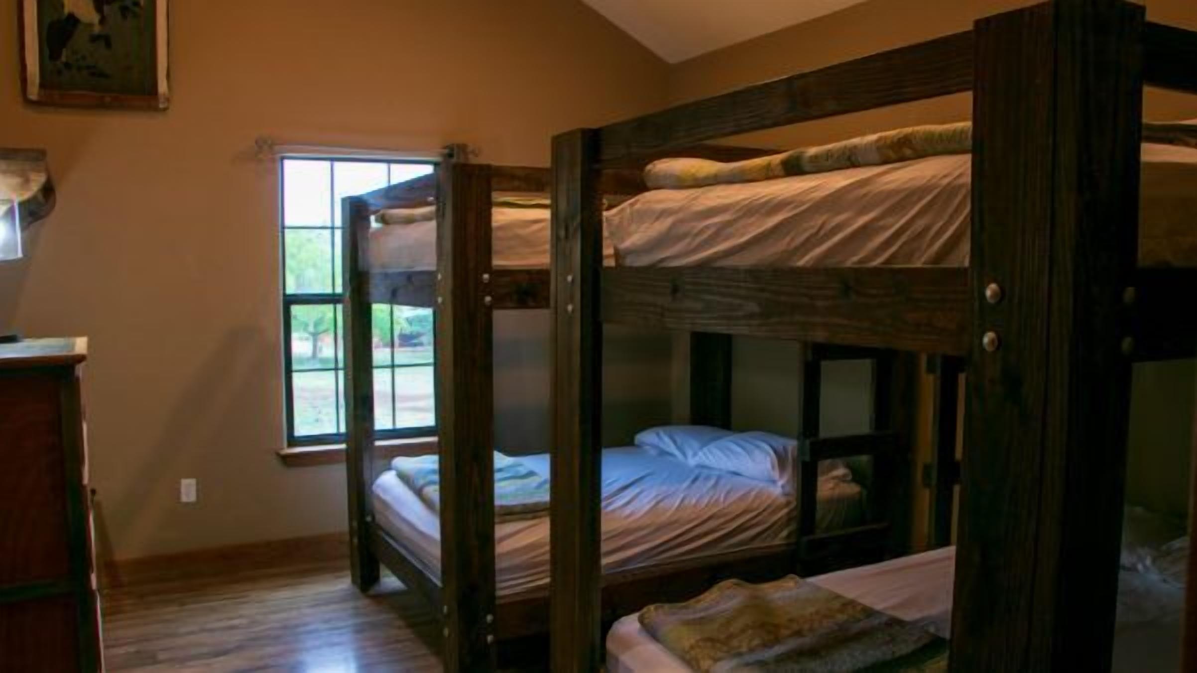 A bunk bed room with a window, wooden furniture, and a painting on the wall.